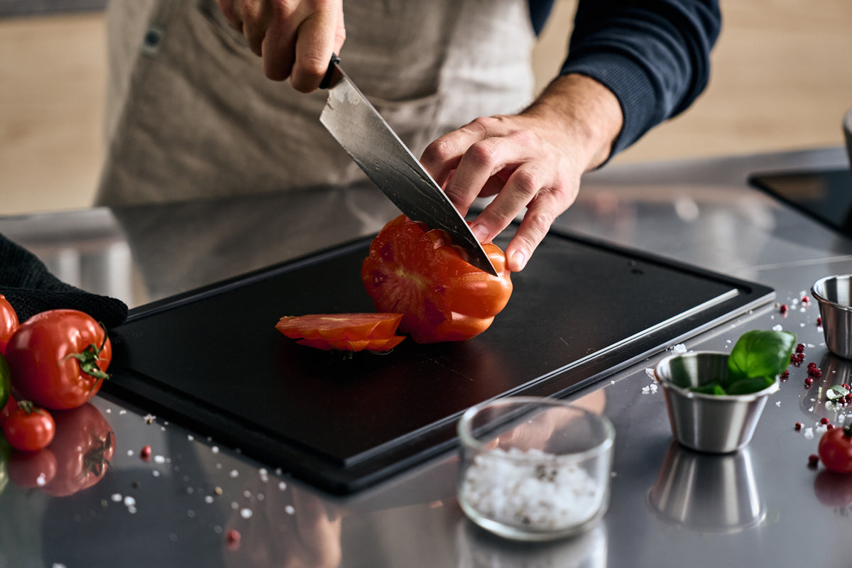 A person cuts a tomato with the precision-engineered Fissler ProCut Chef's Knife 20cm on a simple, modern kitchen counter.