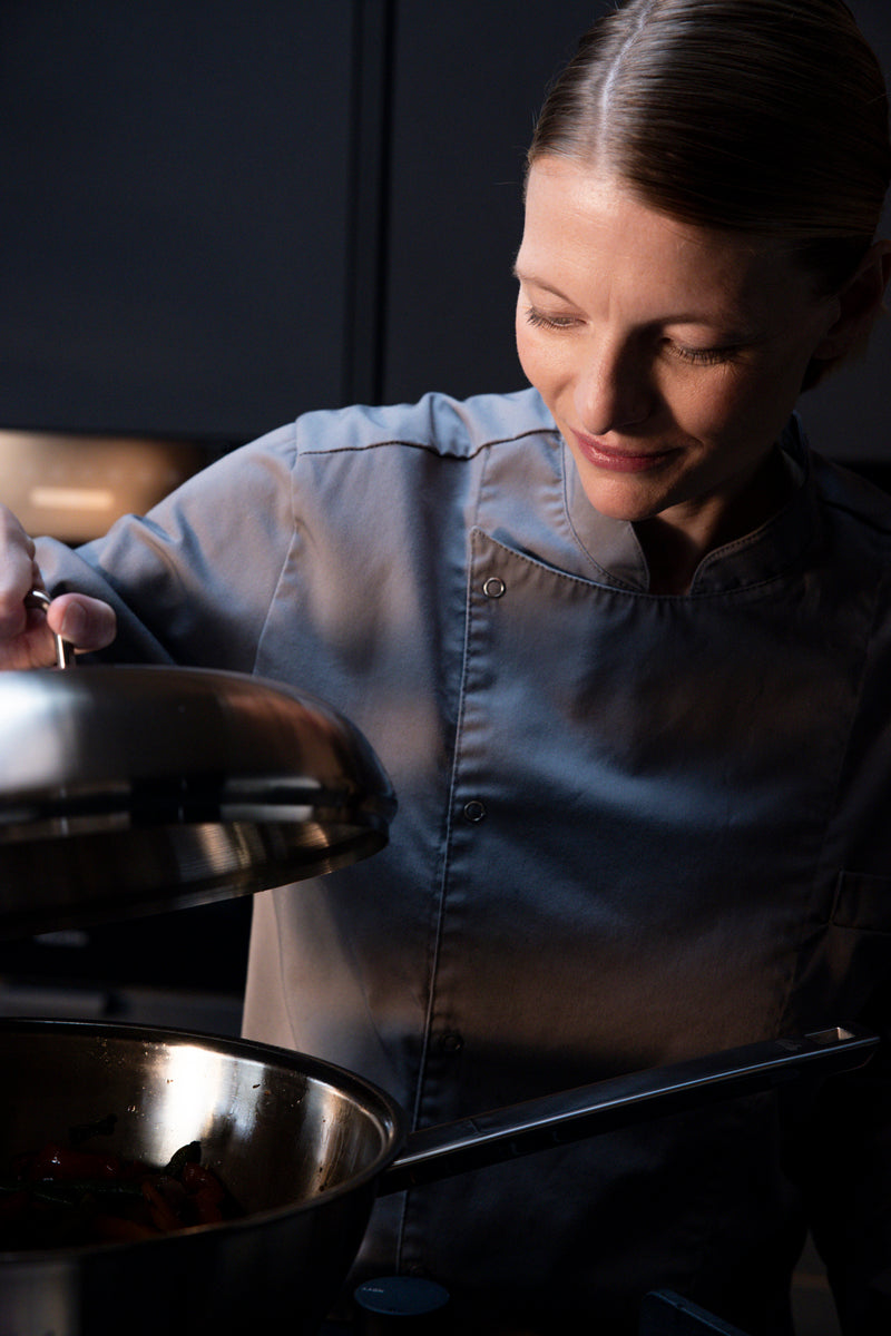 Ein Chefkoch hebt den Deckel eines Fissler Original-Profi Collection® Woks 32cm, der Präzision und zeitloses Design in einer modernen Küche demonstriert.