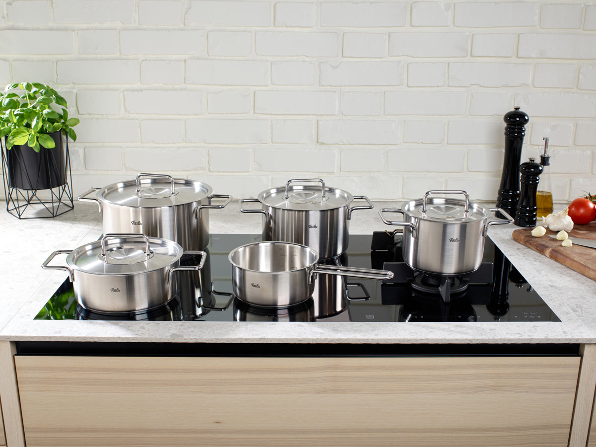 Fissler Pure Collection® Töpfe und Ceratal® Evo Comfort Pan 24 cm auf schwarzem Induktionskochfeld; moderne Küche, frische Kräuter, Gemüse.