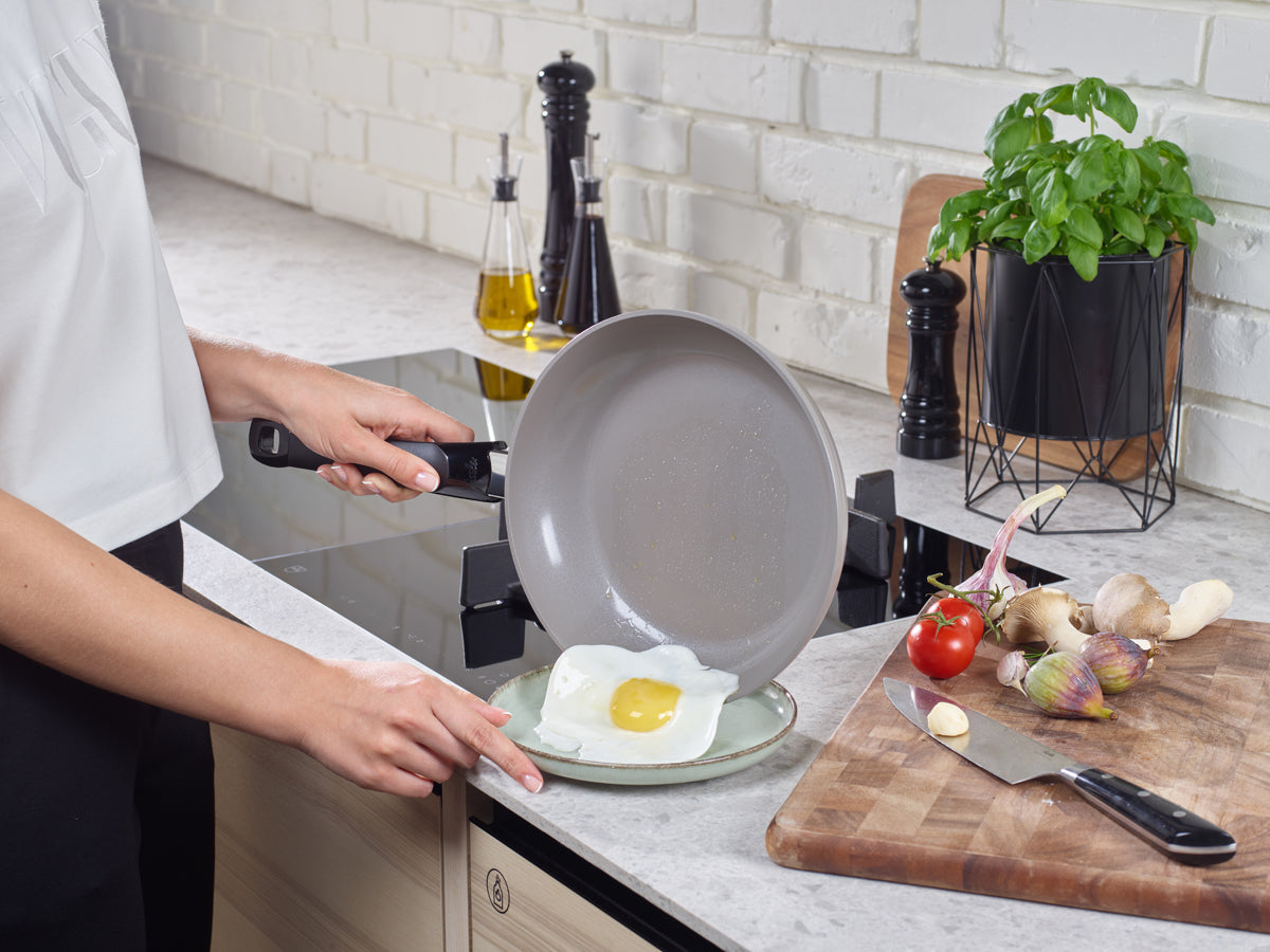 In einer modernen Küche gleitet ein Spiegelei aus dem Fissler Ceratal® Classic Pfannenset auf einen Teller, daneben Fissler Qualitätswerkzeuge.