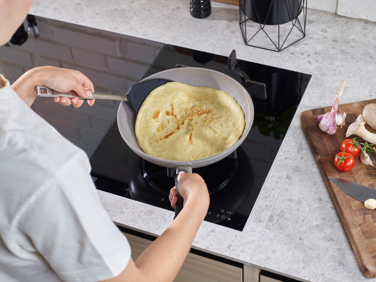 Zubereitung eines Crêpes in einer Fissler Ceratal® Classic Pfanne auf dem Herd; frisches Gemüse und Pilze auf dem Schneidebrett daneben.