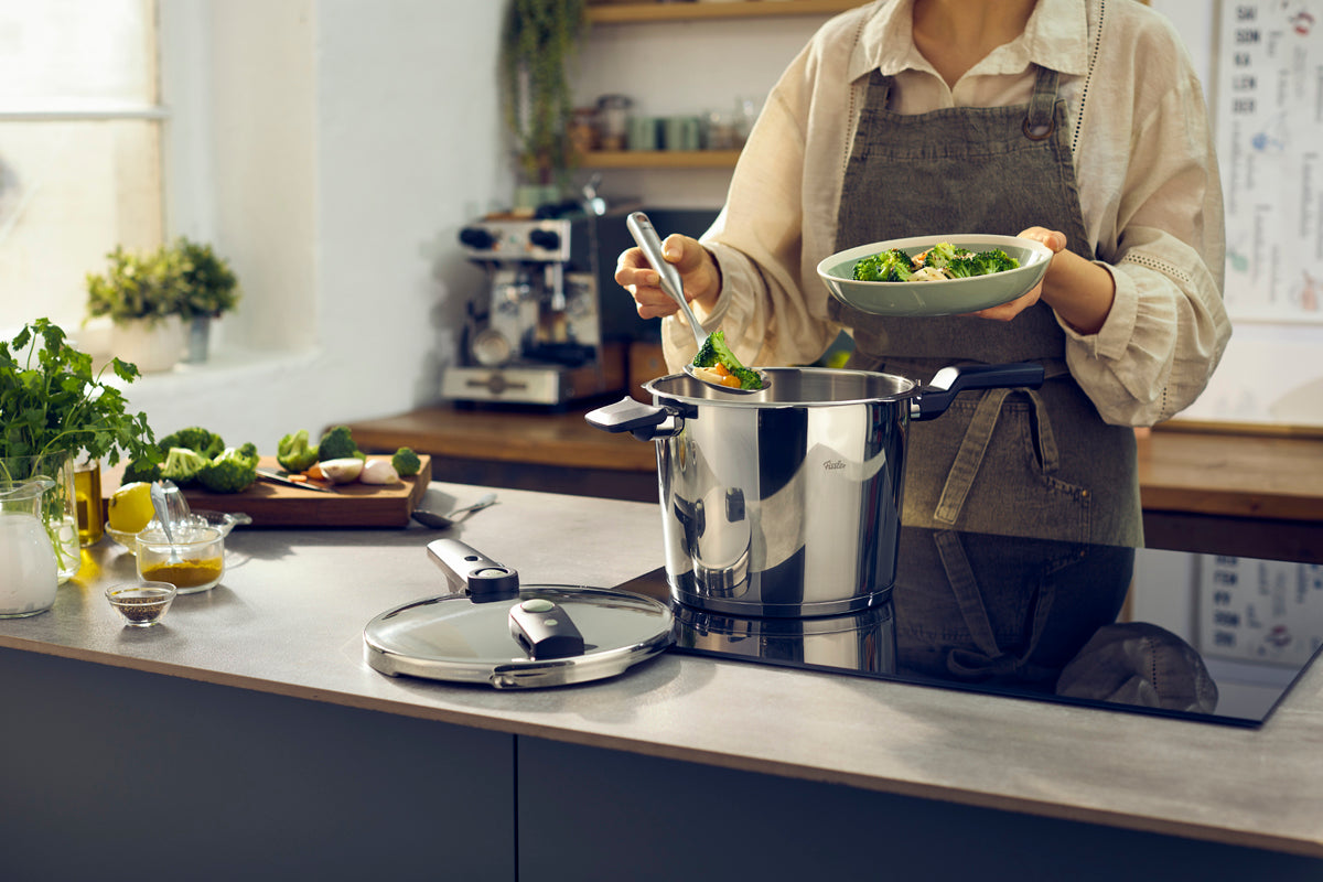 In einer modernen Küche wird das Essen aus dem Fissler Vitaquick® Elemental Schnellkochtopf-Set serviert; auf der Theke stehen frische Produkte.