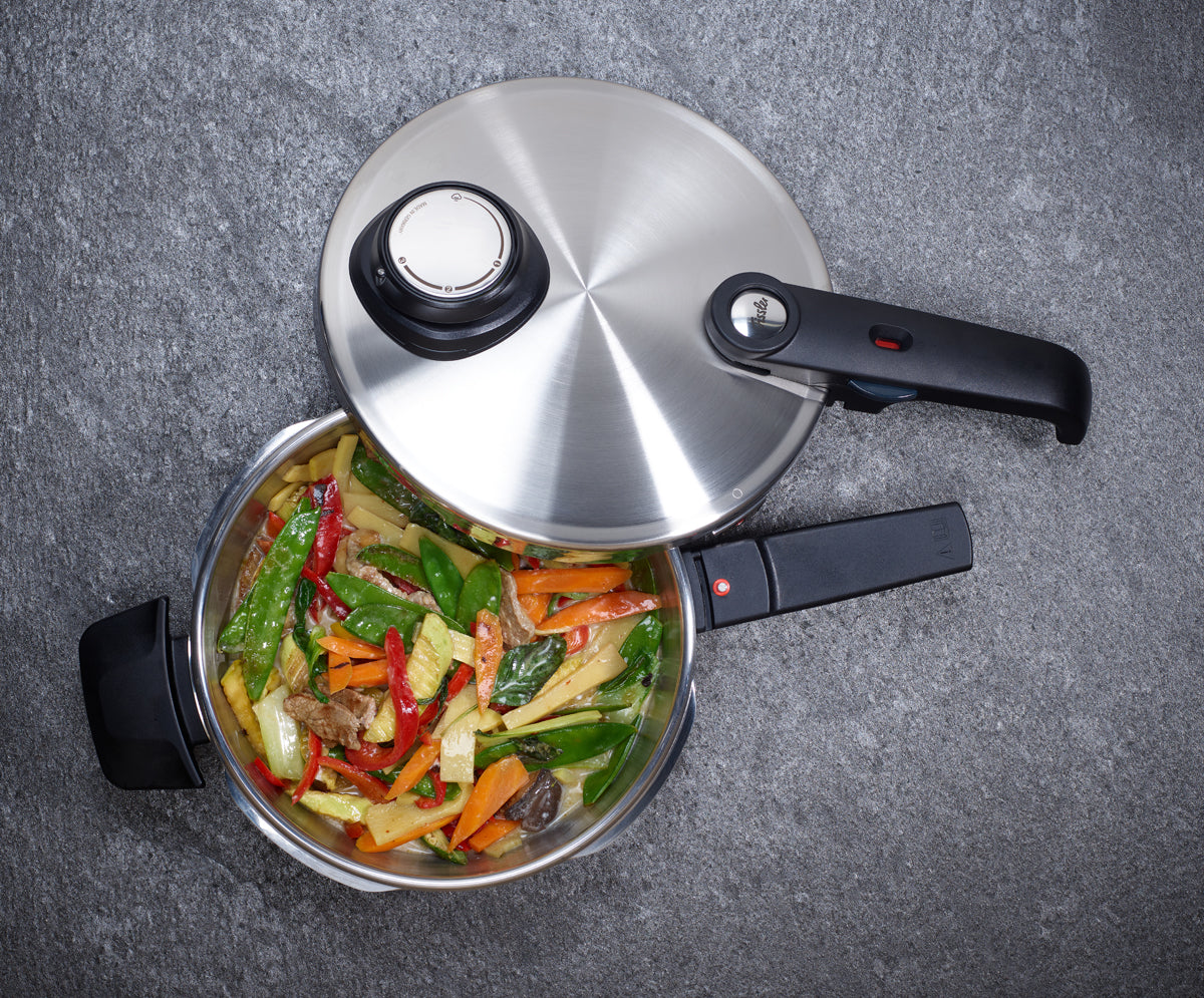 Die Fissler Vitavit® Premium-Schnellbratpfanne aus hochwertigem Edelstahl 18/10, ausgestattet mit einem ergonomisch geformten schwarzen Griff, ist teilweise geöffnet und präsentiert farbenfrohe gebratene Gemüsestreifen sowie zartes Rindfleisch – ein Beispiel für präzises Kochen auf einer edlen, grauen, strukturierten Oberfläche. Die Innovation und das zeitlose Design von Fissler unterstreichen die Qualität „Made in Germany“.