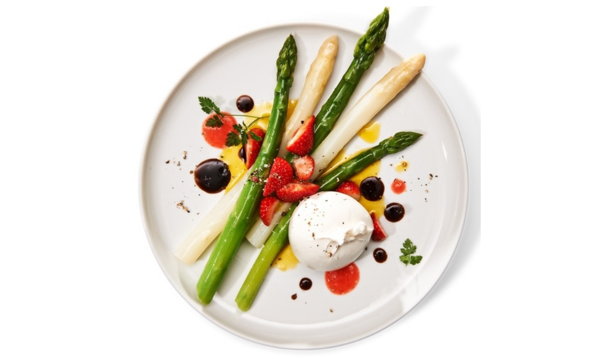 Auf einem weißen Teller werden Spargel, Erdbeeren, Burrata und Kräuter präsentiert - zubereitet mit Fissler Kochgeschirr für perfekte Präzision und Stil.