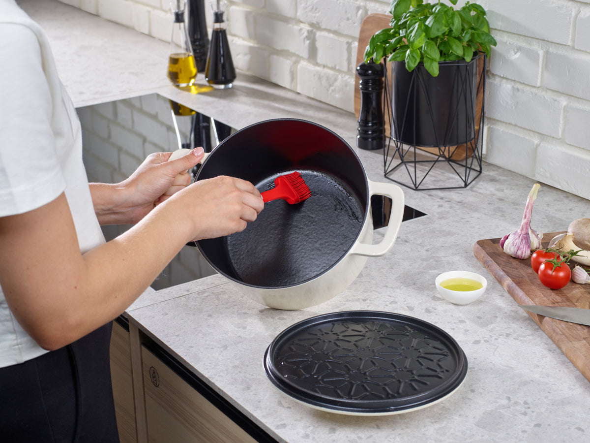 Pinselöl in einem Fissler Moments Gusseisen Topf. Moderne Küche mit Gemüse, Brett und Werkzeug-Präzision "Made in Germany".
