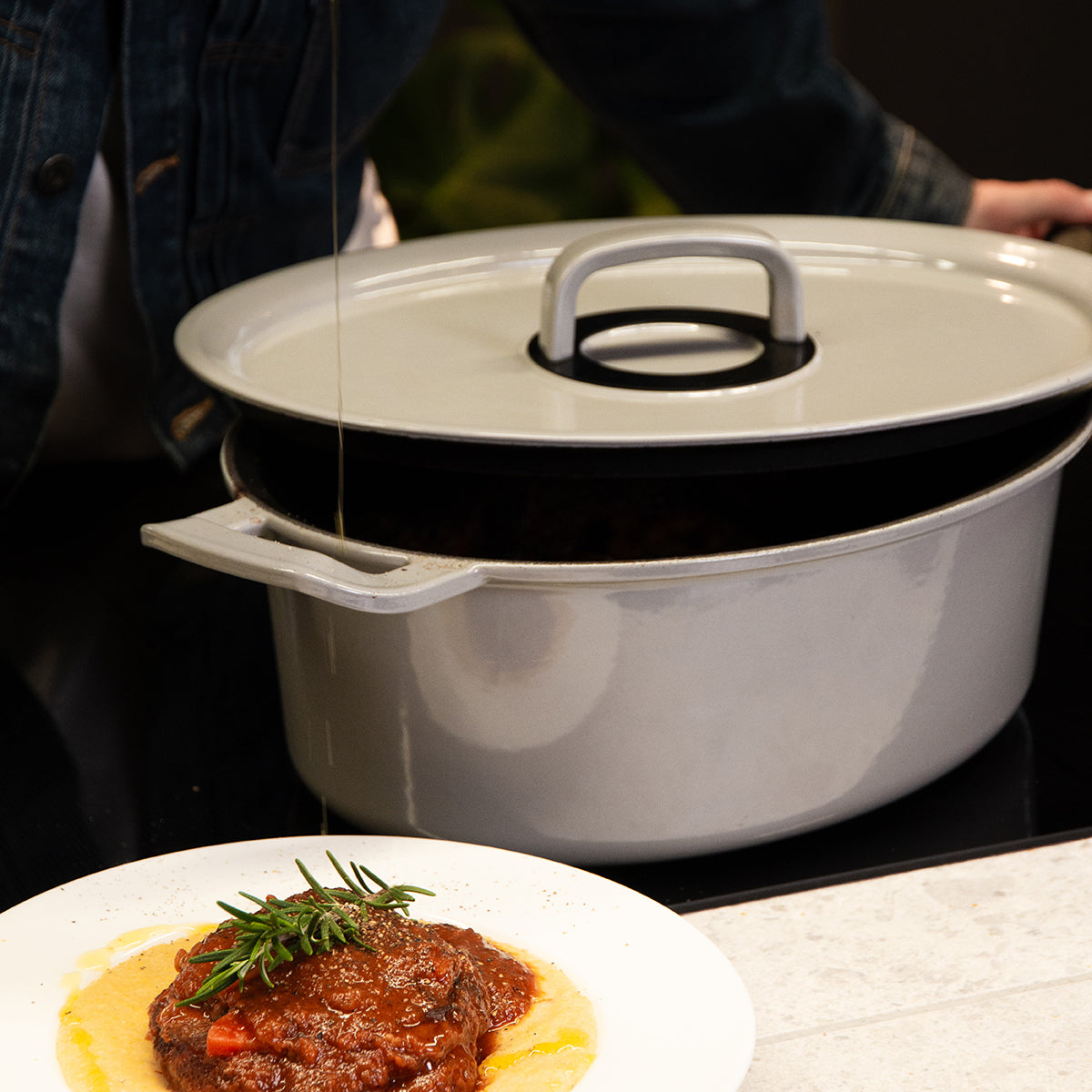Oil is poured over a rosemary-lacquered dish, behind it stands a Fissler cast iron roaster, showcasing German precision and design.