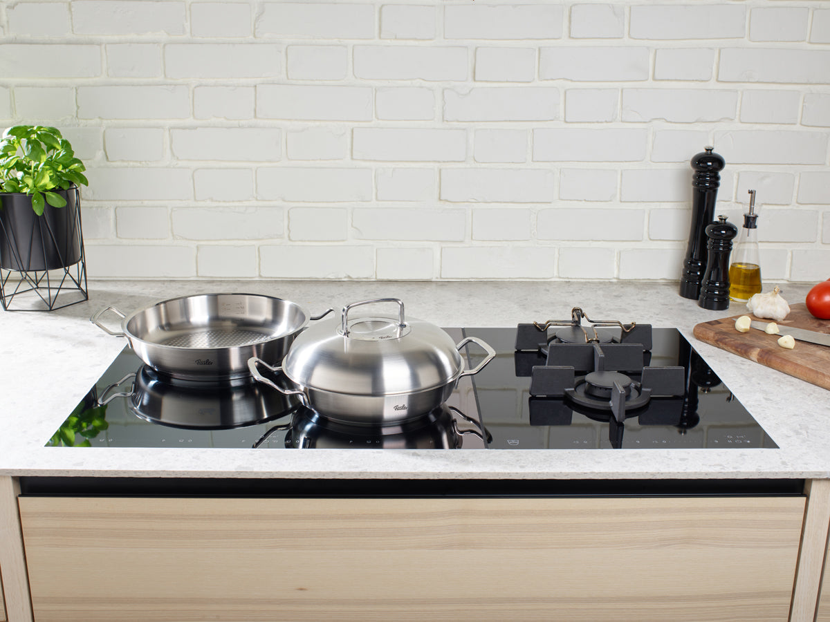 Fissler Original-Profi Collection® Hochraumdeckel und Edelstahlpfannen auf einem schlanken Kochfeld - zeitloses deutsches Design und Qualität.