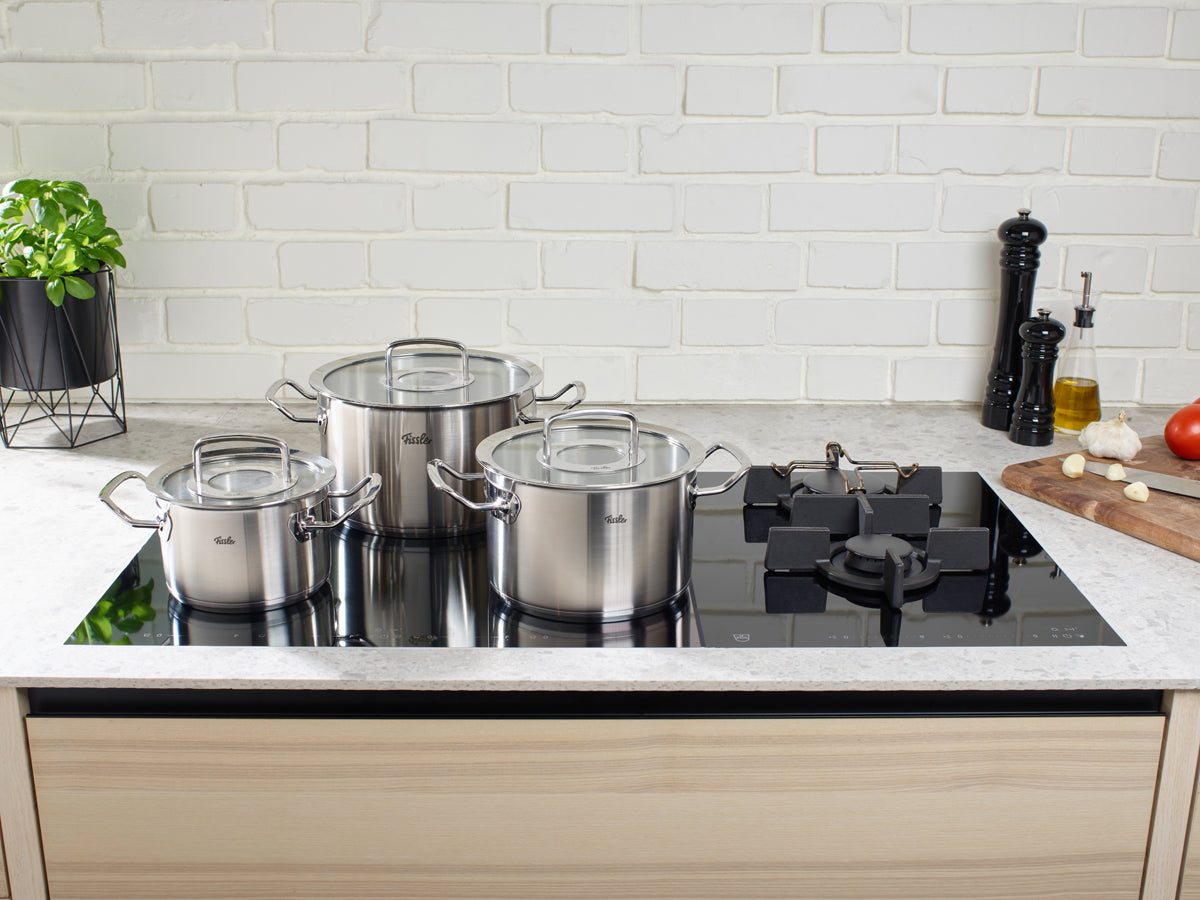 Fissler Original-Profi Collection® 5-teiliges Topfset auf einem eleganten schwarzen Herd, mit frischen Zutaten, in einer modernen Küche.