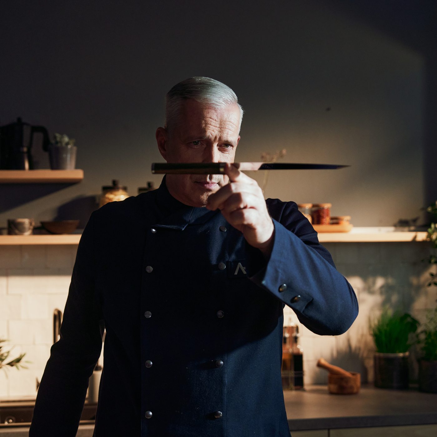 Ein Koch in einer modernen Küche begutachtet ein Fissler-Messer, das für deutsche Präzision und zeitloses Design unter den Premium-Kochgeräten steht.