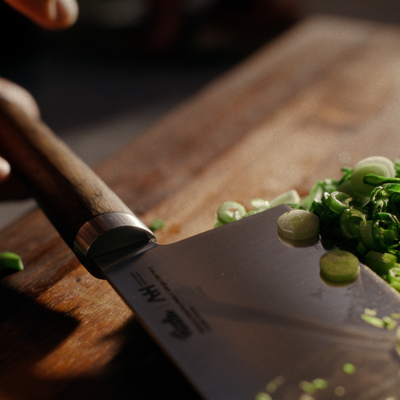 Das präzise gefertigte Fissler-Kochmesser schneidet grüne Zwiebeln auf einem hölzernen Schneidebrett, wobei das Sonnenlicht jedes frische Detail beleuchtet.