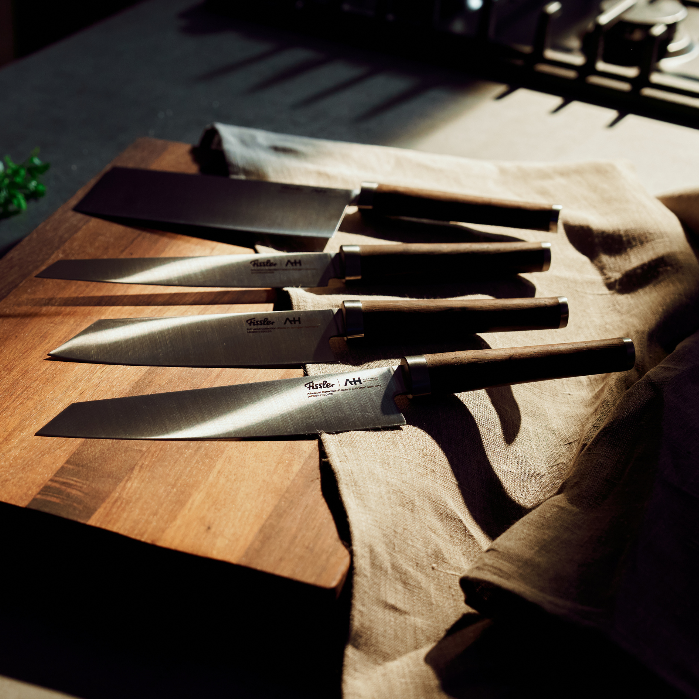 Fissler Kochmesser mit dunklen Griffen auf einem Holzbrett und beigem Tuch, sonnenbeschienen in einer Küche, zeigen deutsche Präzision und zeitloses Design.