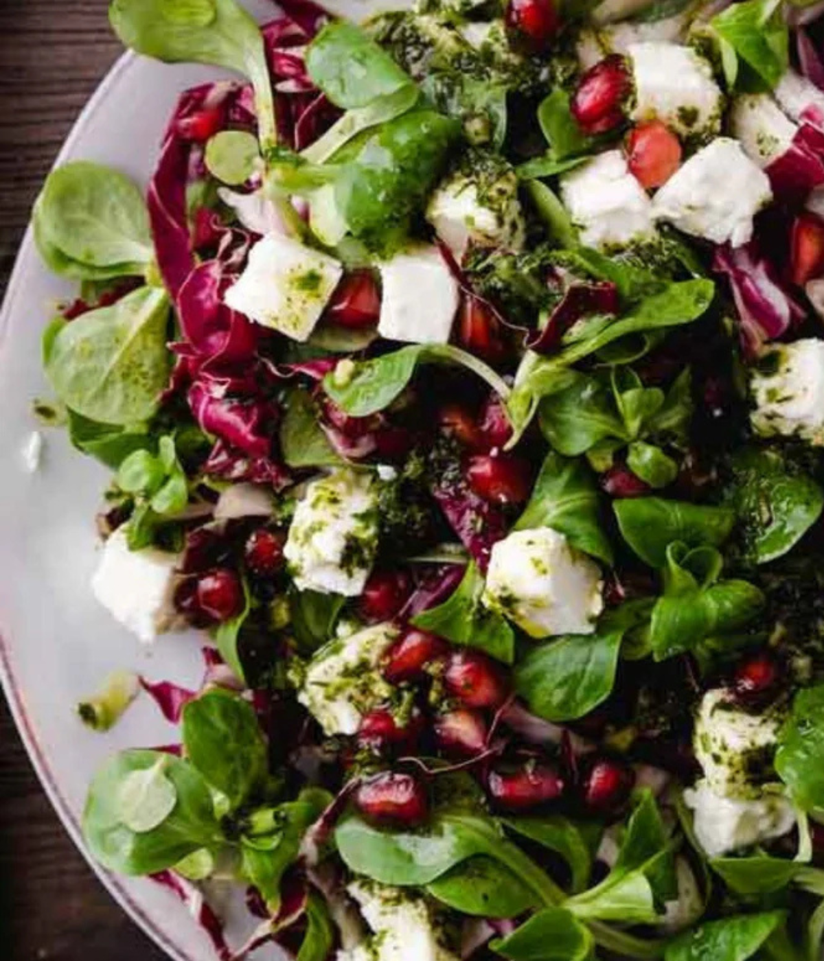 Ein lebendiger Salat aus Grünzeug, Radicchio, Granatapfel und Feta auf einem weißen Teller - präsentiert im zeitlosen deutschen Design von Fissler.
