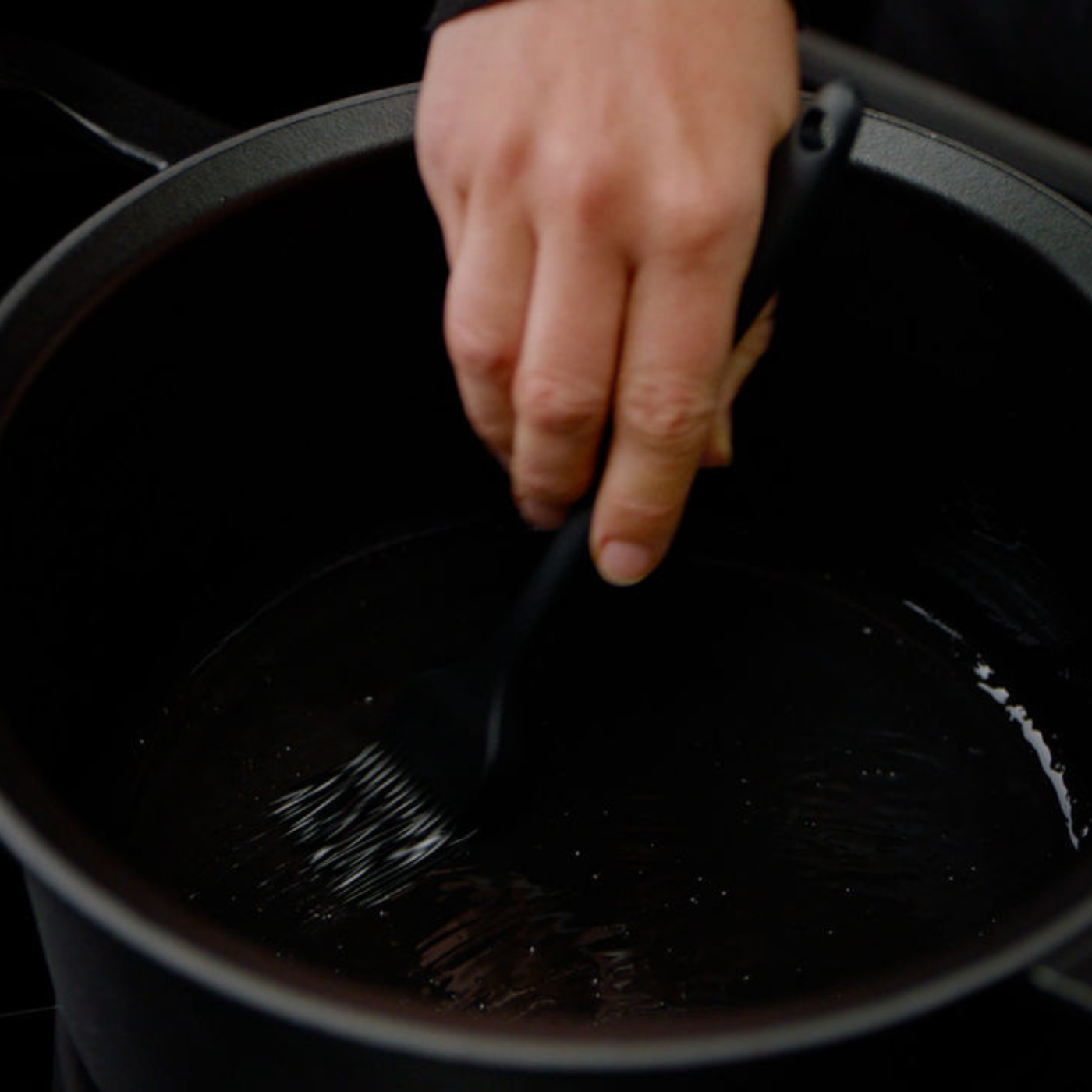Eine Hand benutzt einen Fissler-Pinsel, um das Öl in einem hochwertigen schwarzen Fissler-Topf aufzutragen und das langlebige Kochgeschirr für das Präzisionskochen vorzubereiten.
