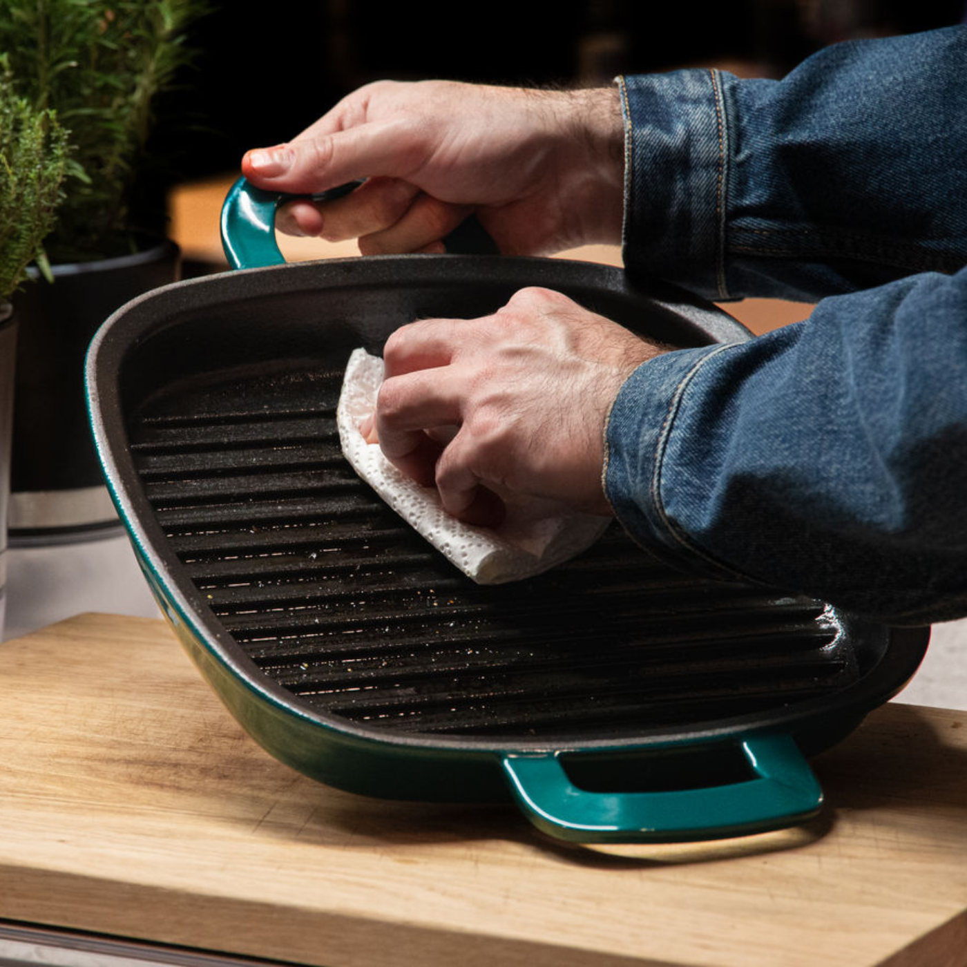 Eine Person in Jeansjacke reinigt eine hochwertige gusseiserne Grillpfanne auf Holz, in der Nähe die Qualität und das zeitlose deutsche Design von Fissler.