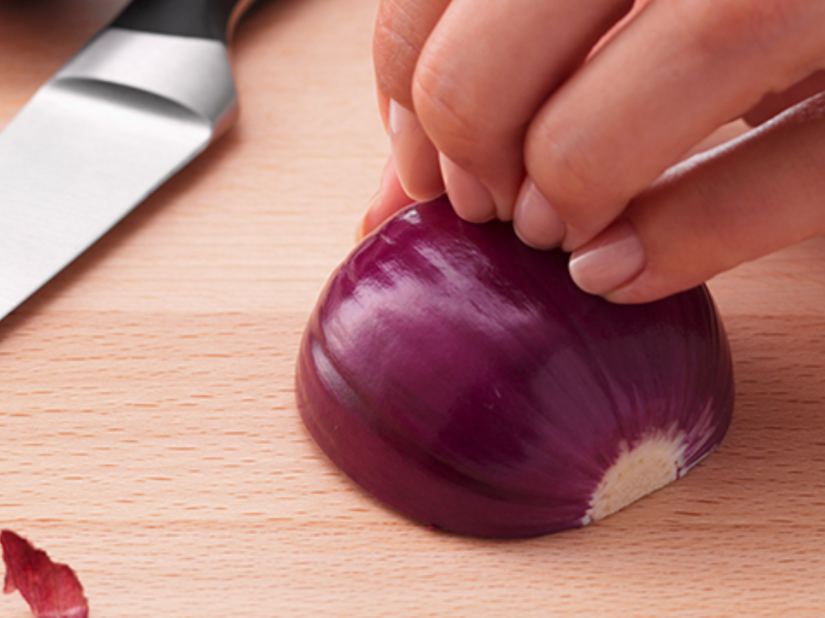 A hand holds a halved red onion on a wooden board, next to it lies a precision-crafted Fissler kitchen knife - timeless German design.