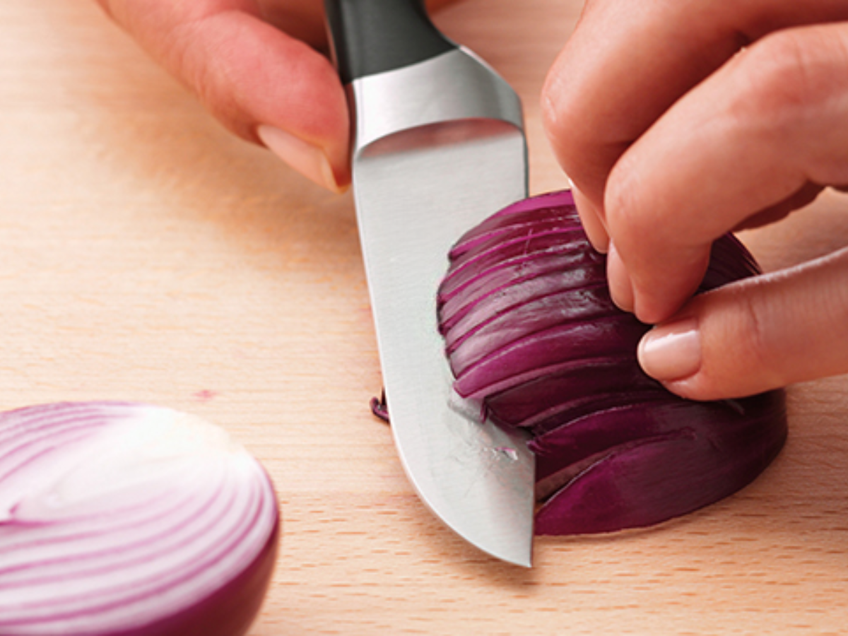 A person expertly cuts a red onion on a wooden cutting board with a Fissler knife, showcasing German precision and quality craftsmanship.