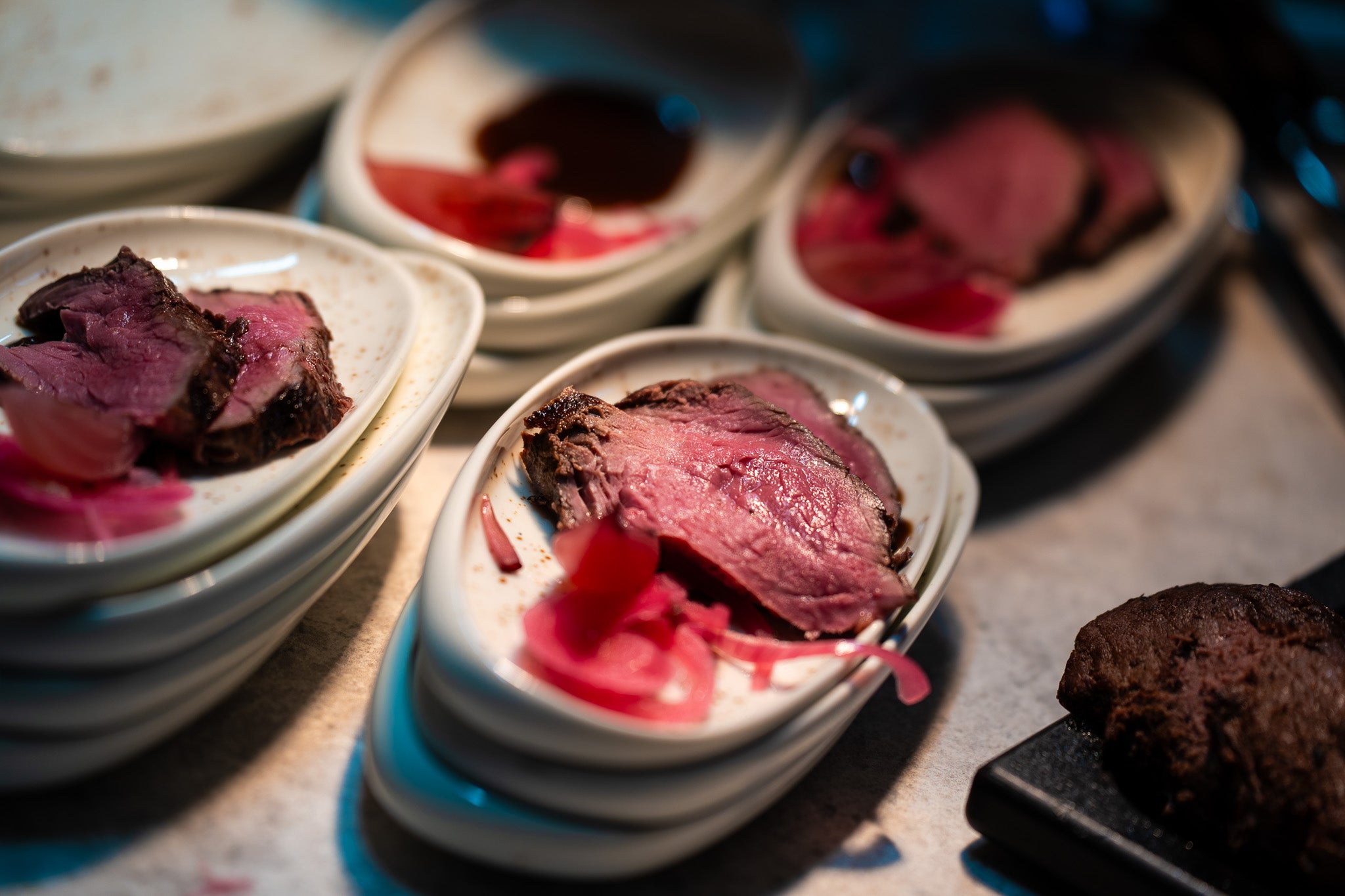 Halb durchgebratenes Roastbeef mit eingelegten Zwiebeln auf weißen Tellern, elegant auf einer Arbeitsplatte neben Fissler-Kochgeschirr angerichtet.
