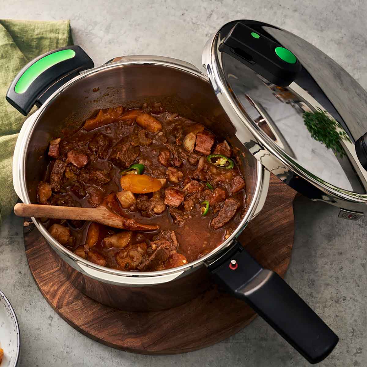 Fissler Vitaquick® Green Pressure Cooker, open with beef goulash inside, on a wooden board. Lid next to it; sleek German design, nutritious results.