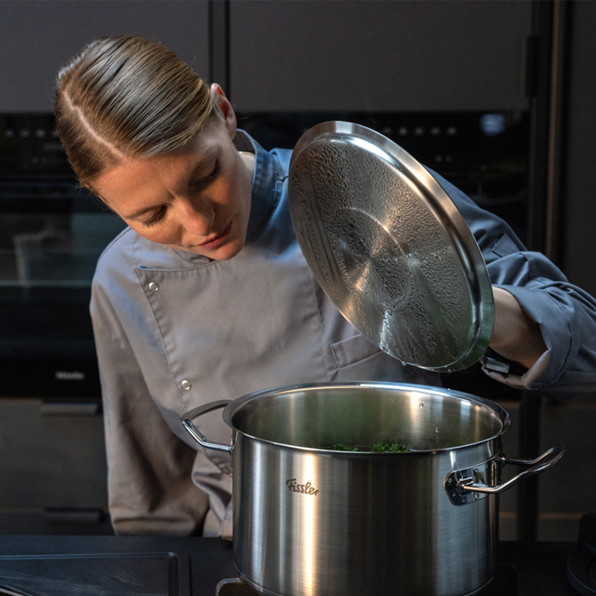 Ein Koch in einer modernen Küche hebt den Deckel des Edelstahltopfes der Original-Profi-Collection® von Fissler, bekannt für deutsche Präzision.