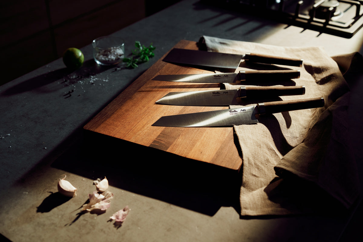 Fissler PrimeCut 17cm Santoku knife on a wooden board with garlic, lime, and sunlight - modern German quality meets timeless design.
