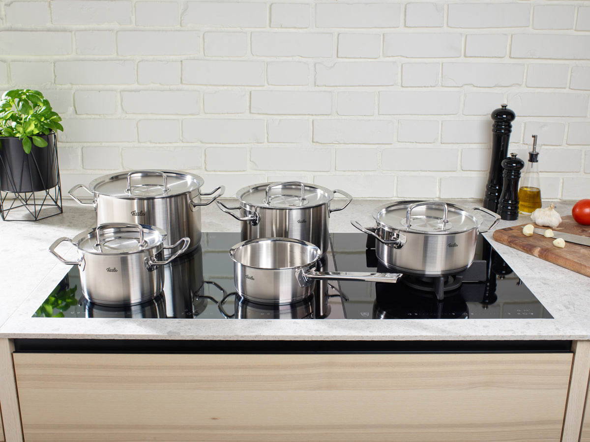 Fissler Original-Profi Collection® 5-teiliges Edelstahlset mit Deckeln auf dem Herd, zeitloses Design, German made, Gemüse und Akzente in der Nähe.