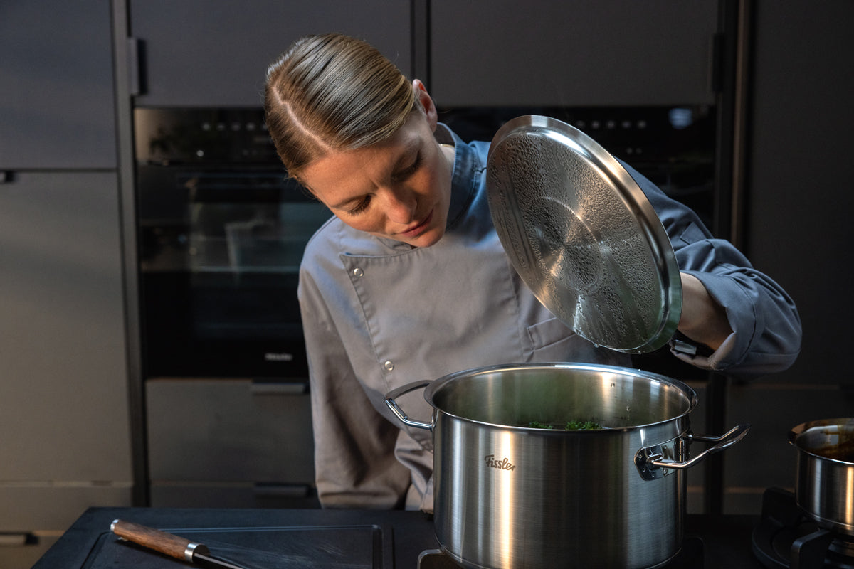 Ein Koch prüft eine Mahlzeit in einem 5-teiligen Edelstahltopfset der Fissler Original-Profi Collection®, das für deutsche Qualität und Design steht.