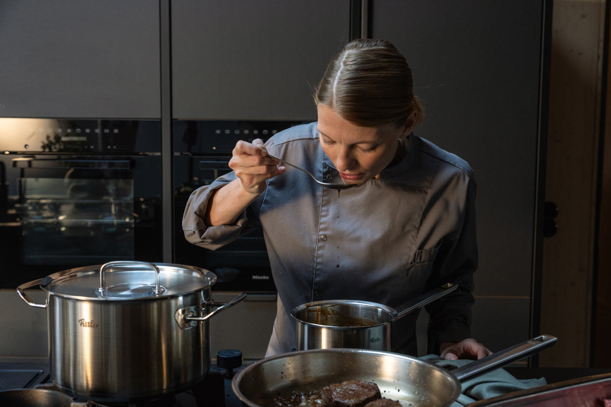 A chef tastes food over a 5-piece set of the Fissler Original-Profi Collection®, showcasing the quality of German stainless steel on the stovetop.