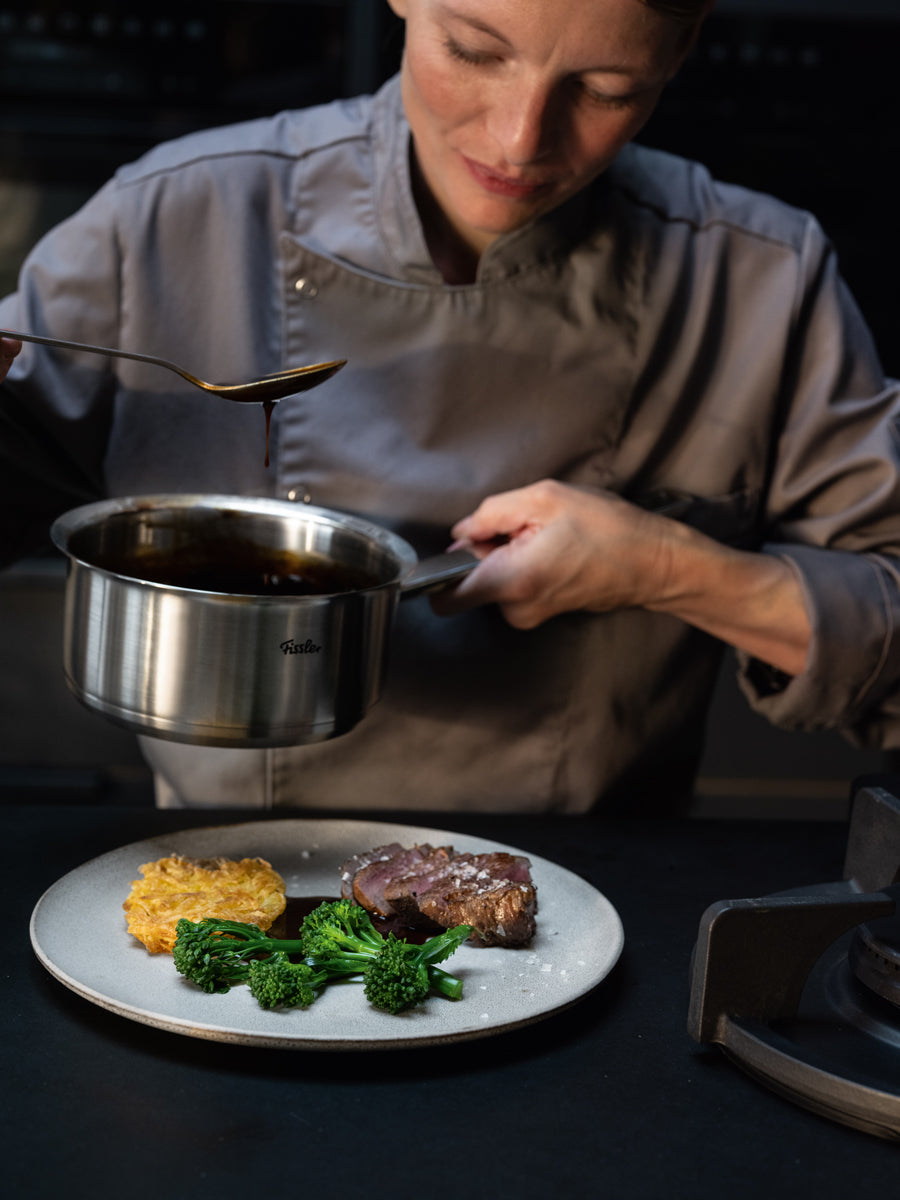 A chef uses the 7-piece Fissler Original-Profi Collection® set to drizzle steak, broccolini, and potato cake with sauce.