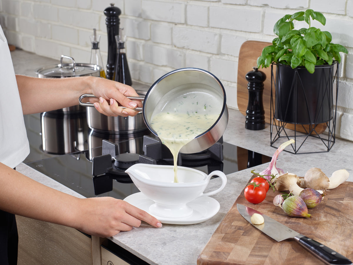 Creamy herb soup served in a bowl, made in a Fissler Pure Collection® pot - timeless German quality - surrounded by fresh vegetables.