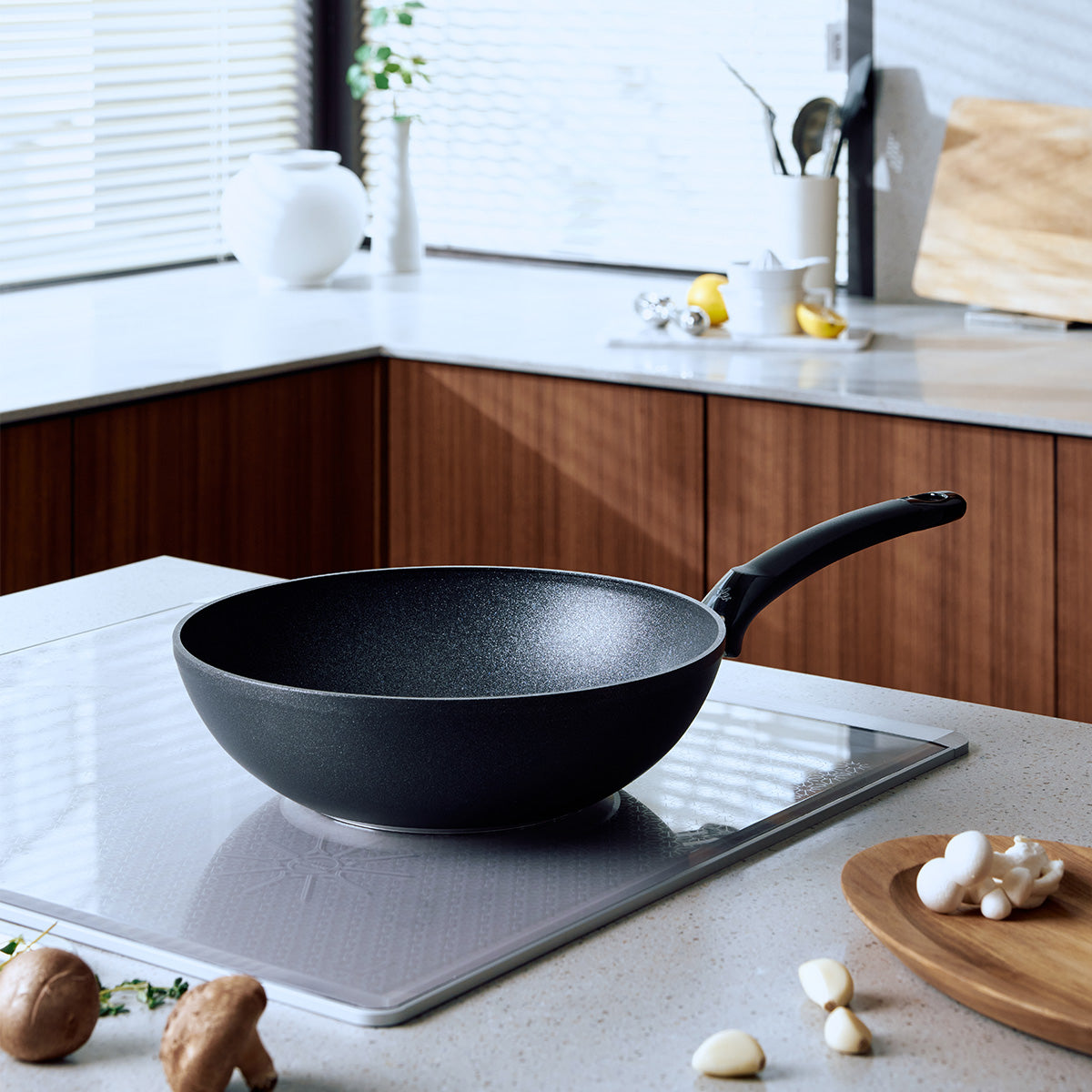 Die Fissler Adamant® Wokpfanne, ausgestattet mit einer langlebigen Antihaftbeschichtung und auf außergewöhnliche Leistung ausgelegt, steht auf einem eleganten Induktionskochfeld in einer hellen Küche mit Holzschränken und durchdacht angeordnetem Küchenzubehör. Diese Szene unterstreicht die seit 1845 bekannte deutsche Präzision, das innovative Design und die langlebige Qualität von Fissler – Merkmale, die sich durch unser gesamtes Sortiment an Töpfen, Pfannen, Schnellkochtöpfen und hochwertigen