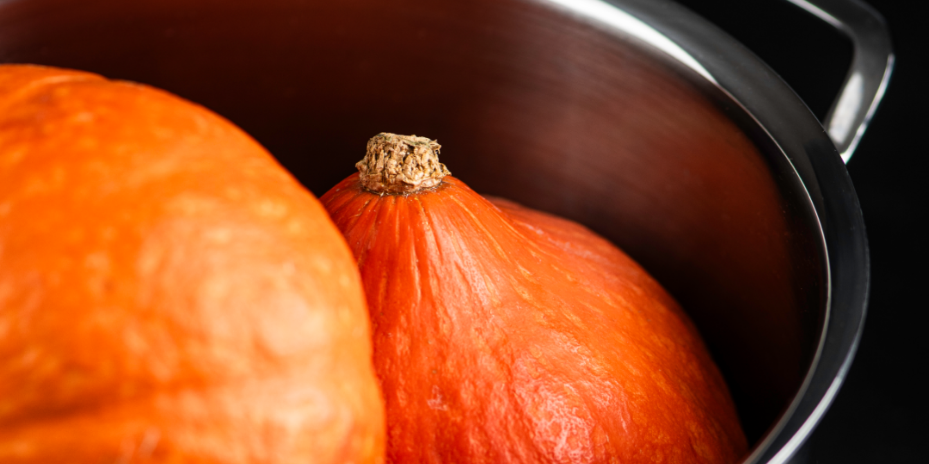 Two glowing pumpkins rest in a high-quality Fissler stainless steel pot with a visible curved rim and handle against a dark background.