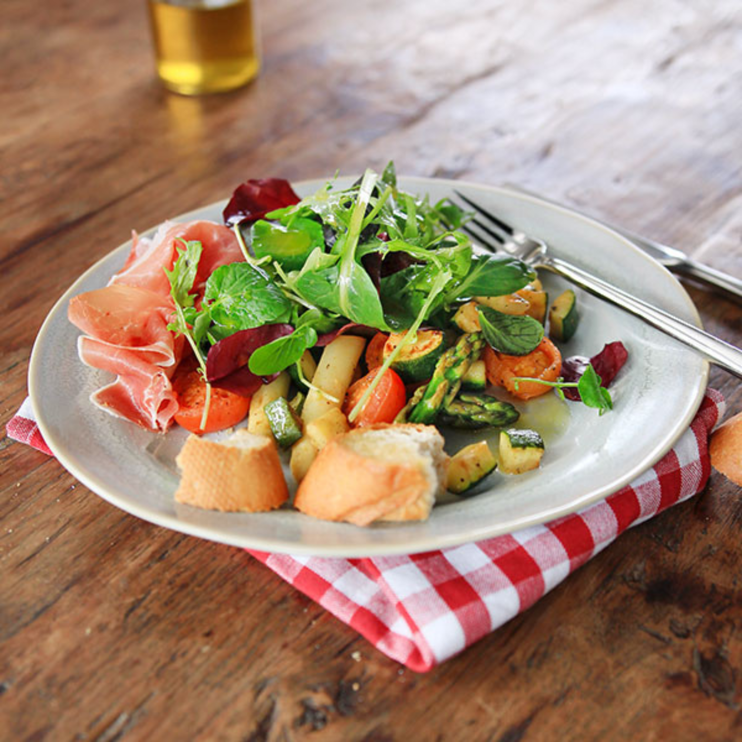 Salat, Gemüse und Baguette auf einem Holztisch mit Fissler-Gabel und -Messer; Bier im Hintergrund, klassisches deutsches Design.