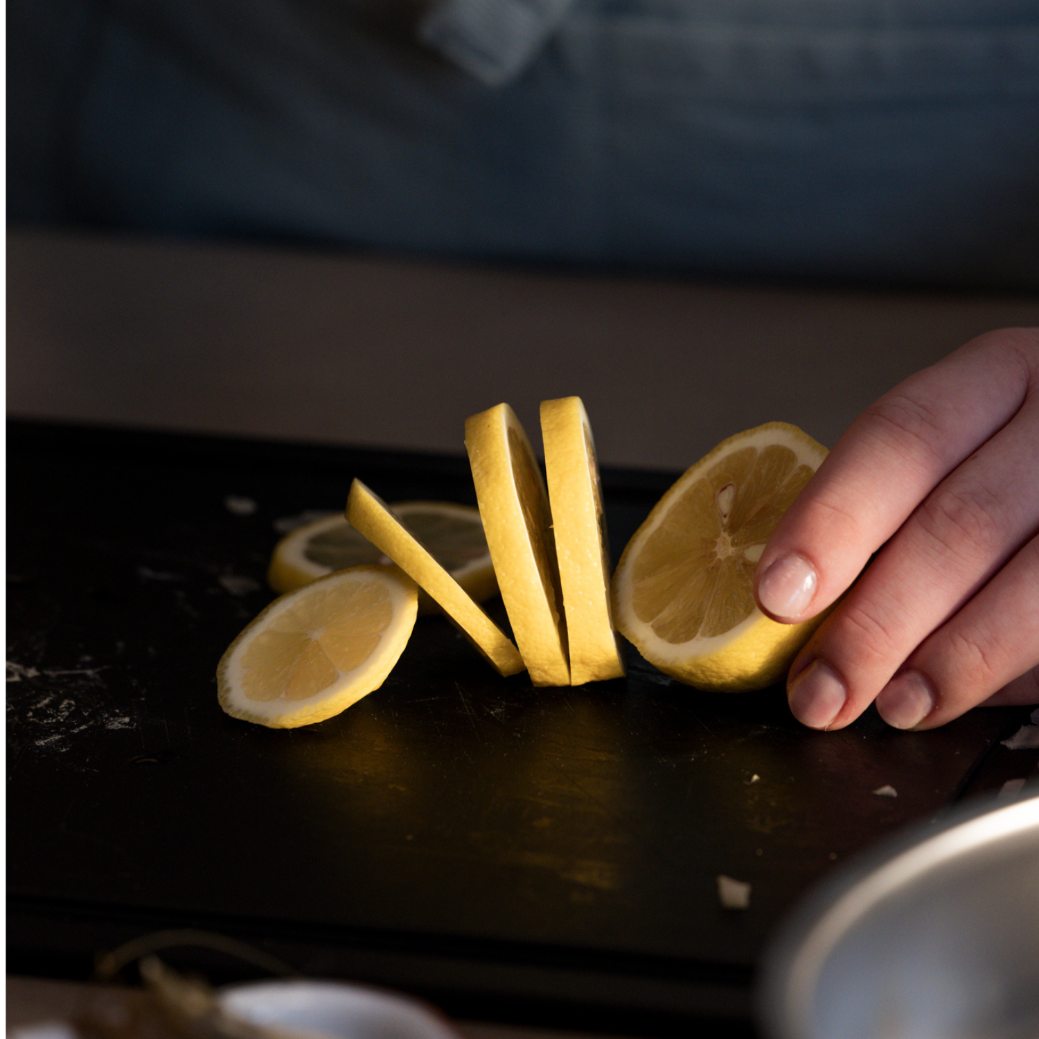 A hand expertly slices a lemon into thin, round pieces on a sleek black cutting board, demonstrating the precision and quality synonymous with Fissler’s German-engineered kitchen accessories.