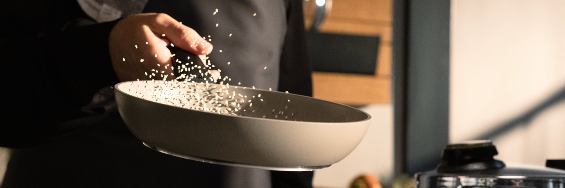 Ein Koch schwenkt Reis in einer hochwertigen Fissler-Edelstahlpfanne, wobei er Präzision und Qualität unter Beweis stellt, während die Körner in der sonnenbeschienenen Luft schwimmen.