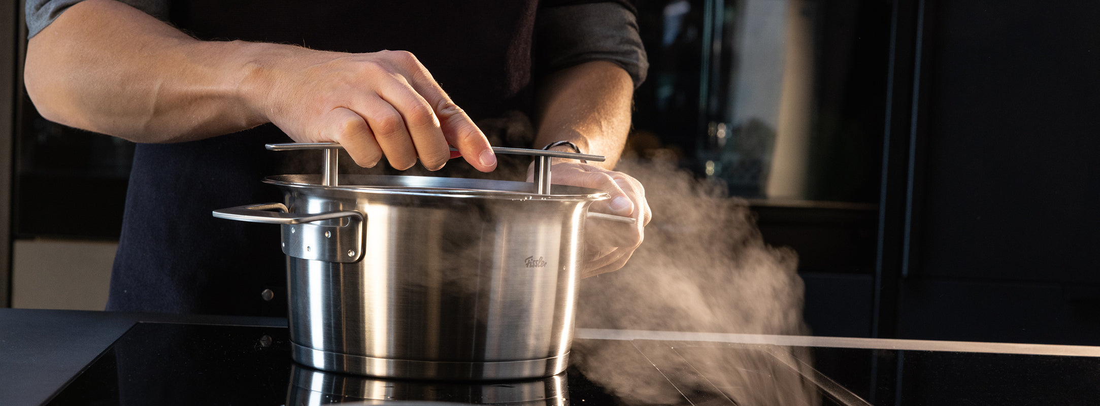 Eine Person hebt den Deckel eines in Deutschland gefertigten Fissler-Edelstahltopfs, aus dem Dampf aufsteigt - ein Beweis für die Qualität von Premium-Kochgeschirr.