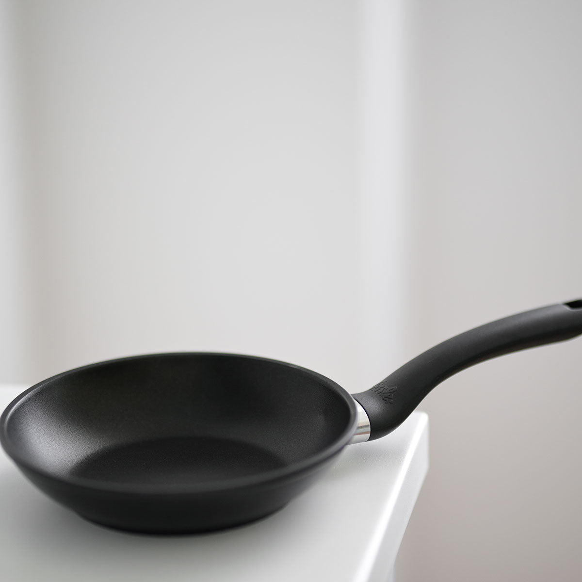 Fissler Cenit® Snack Pan 18 cm, non-stick coating, modern curved handle, on a white surface with a softly blurred background.