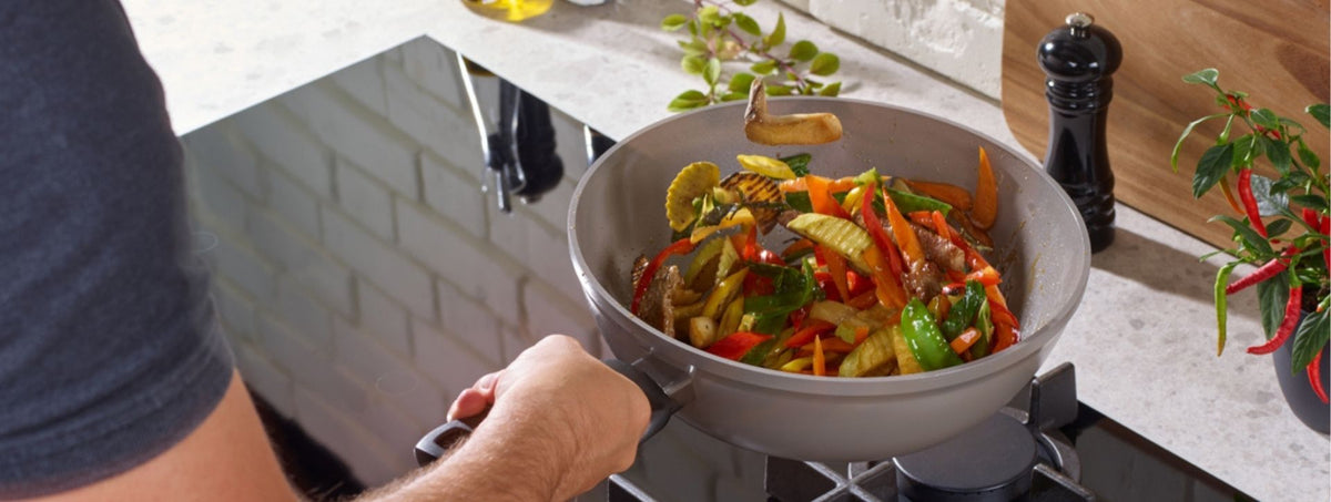 A person prepares a vibrant stir-fry in a Fissler stainless steel pan, with kitchen utensils and fresh ingredients nearby.