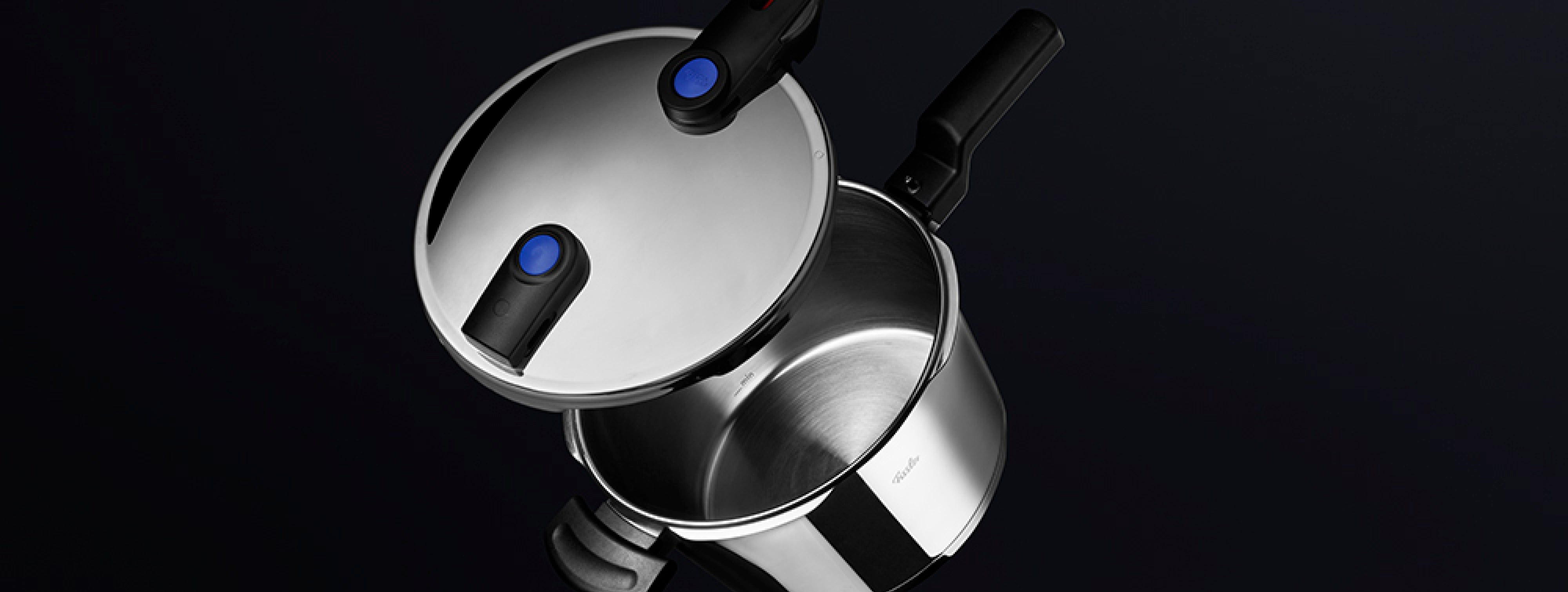 Ein Fissler-Schnellkochtopf aus Edelstahl mit schwarzen Griffen und blauen Sicherheitsknöpfen, teilweise geöffnet, ist ein Beispiel für deutsche Qualität.
