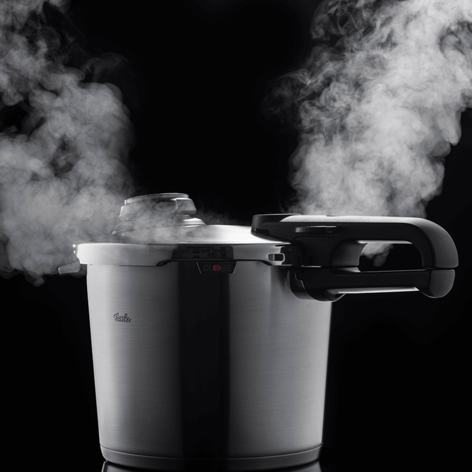 A Fissler stainless steel pressure cooker with black handles releases steam, showcasing German precision and quality against a dark background.