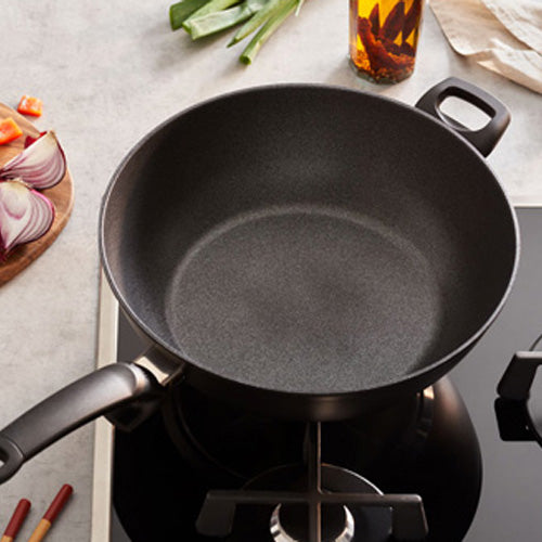 Fissler Adamant® Wok with durable non-stick coating on the stovetop, vegetables and oil nearby - German precision cookware since 1845.