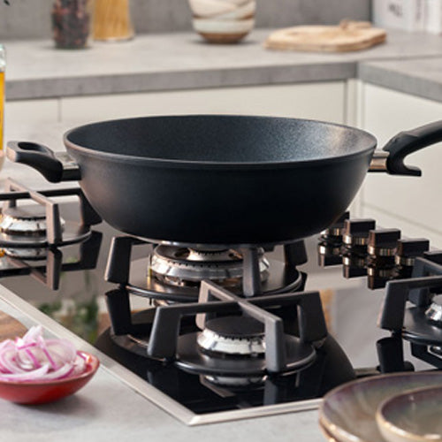 Fissler Adamant® Wok with scratch-resistant coating on a gas stove, demonstrating German precision and durability. Red onions nearby.