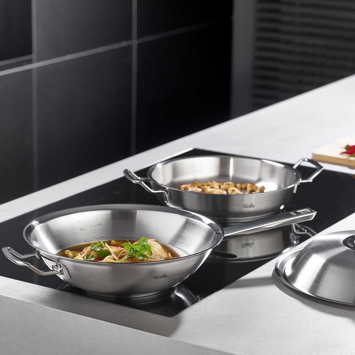 Zwei Fissler-Edelstahltöpfe auf dem Herd - einer mit Gemüseeintopf, einer mit Nudeln; der Deckel des Fissler-Topfes liegt auf dem Tresen daneben.