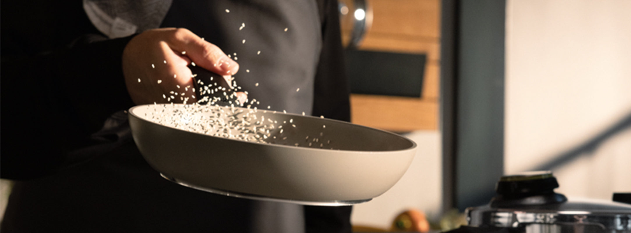 A person skillfully flips white grains, likely rice, in a Fissler beige frying pan over a stove, highlighting the pan's precision engineering as some grains are caught midair. The timeless design and quality craftsmanship of Fissler cookware elevate everyday cooking to an art form.