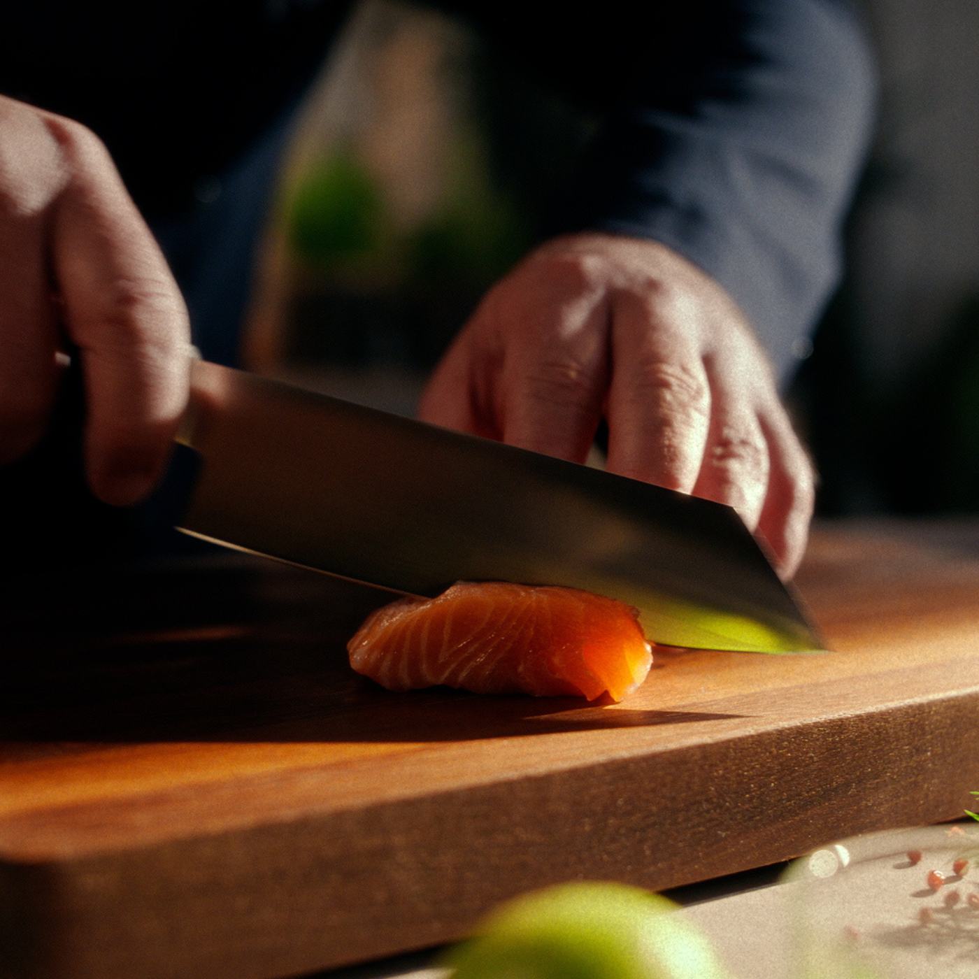 Eine Person schneidet rohen Lachs auf einem Holzbrett mit einem hochwertigen Fissler-Kochmesser präzise in Scheiben, wobei die Handwerkskunst im Vordergrund steht.