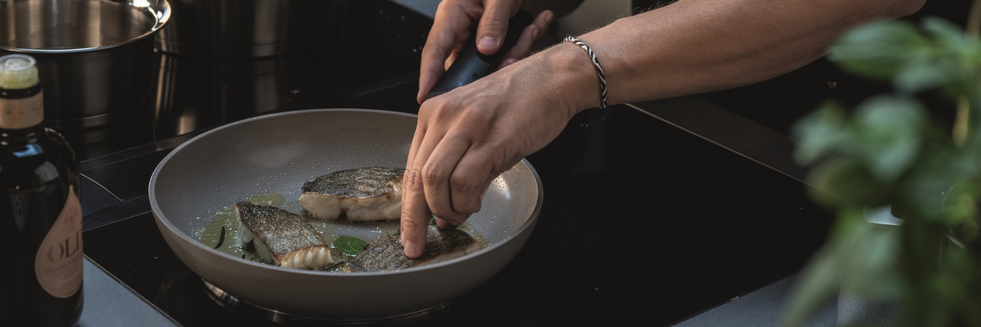 A person arranges fish fillets in a Fissler Frying Pan on the stove, with fresh herbs and a bottle beside the high-quality Cookware.