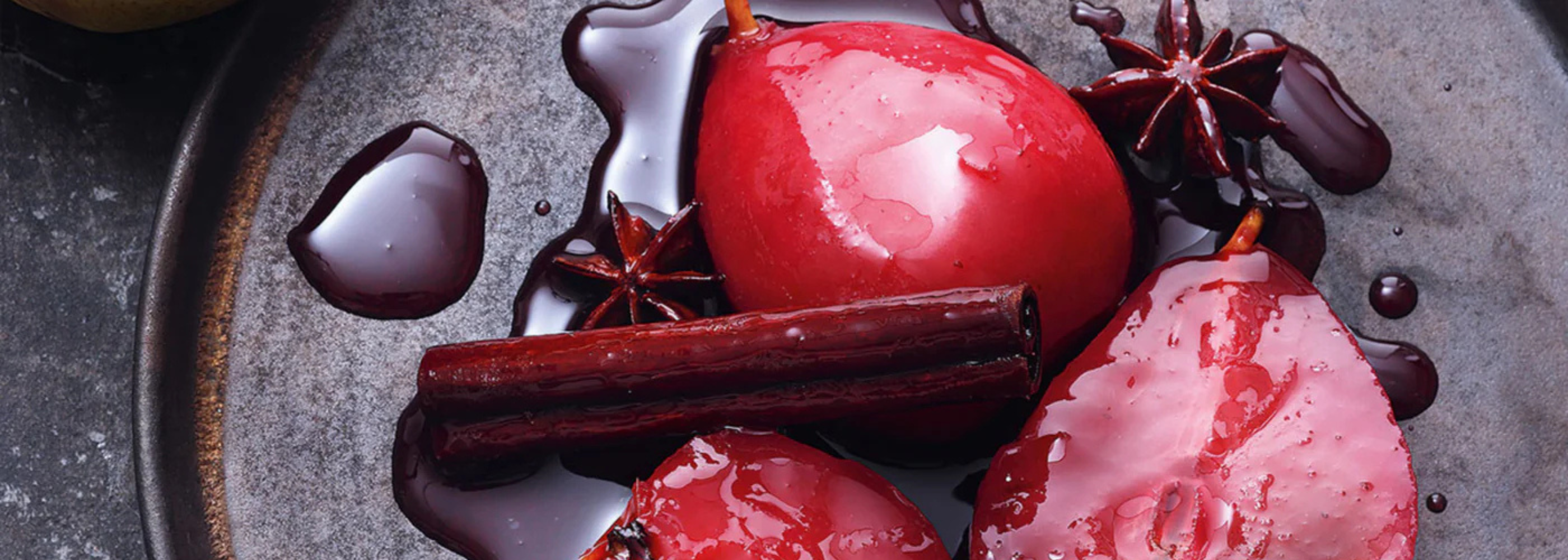 Drei pochierte Birnen in Rotwein mit Sternanis und Zimt, serviert auf einem dunklen Teller, mit reichhaltigem Sirup verfeinert - präzise angerichtet.