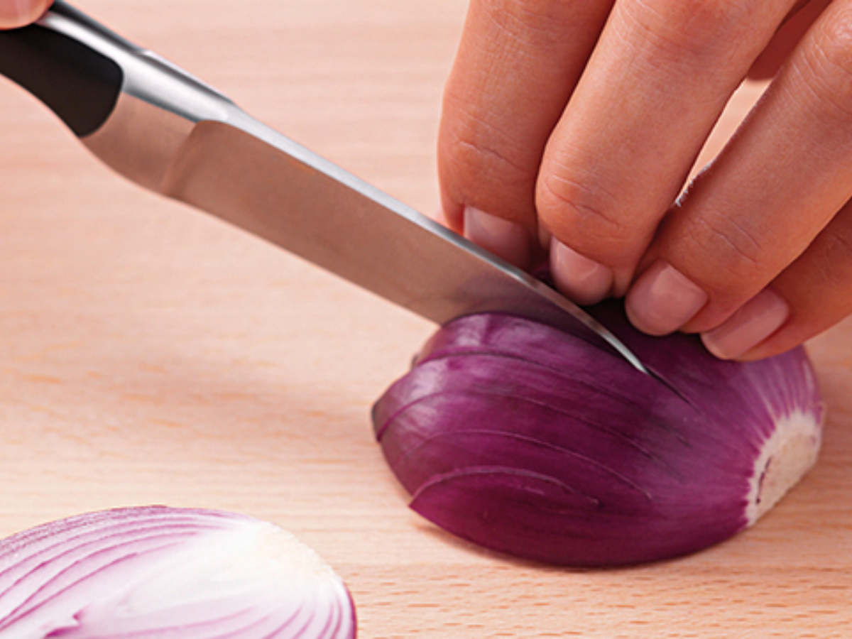 Close-up of a hand expertly slicing a red onion with a precision Fissler knife on a wooden cutting board.