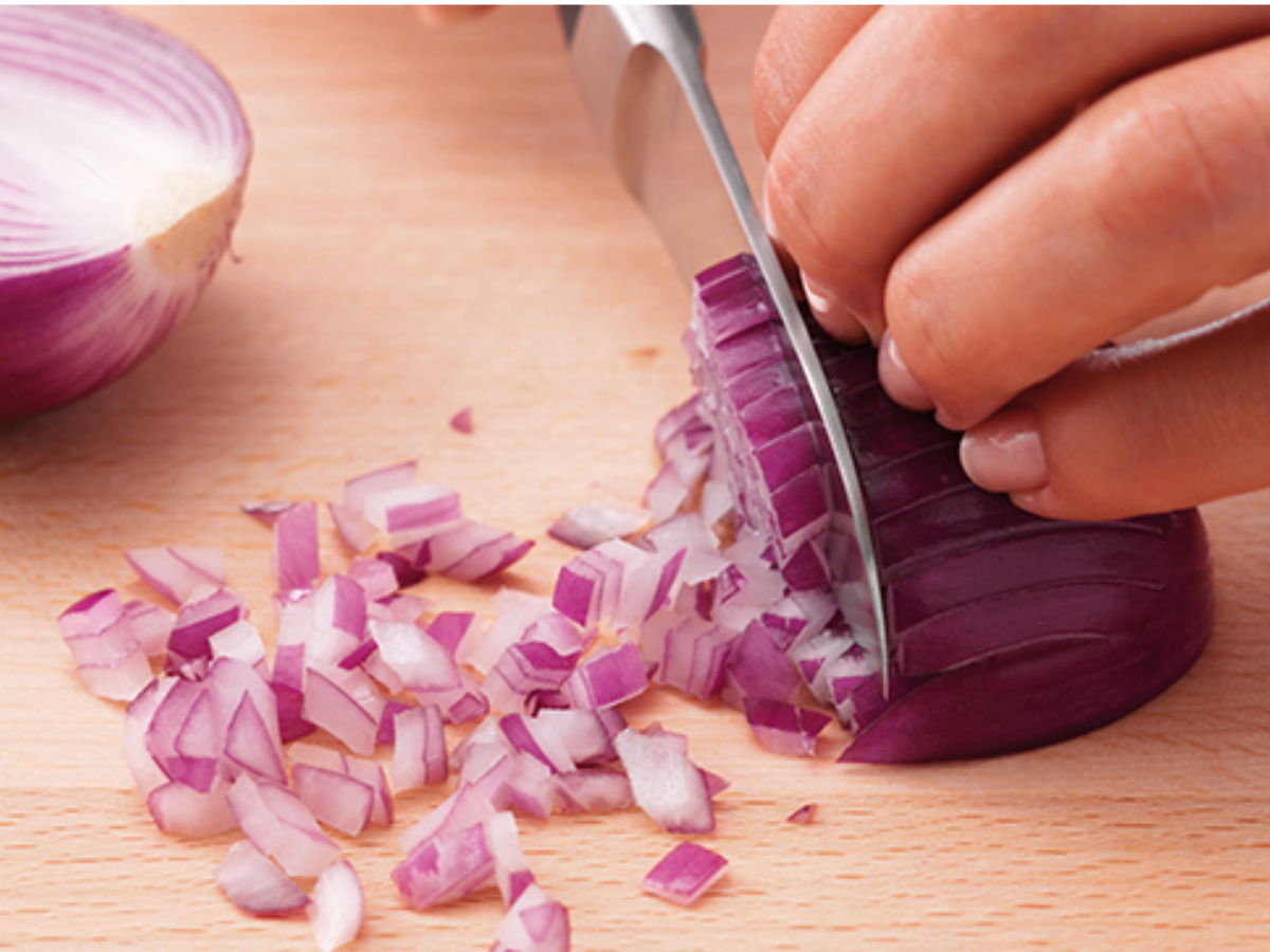 A person expertly slices a red onion on a wooden cutting board, showcasing the Fissler precision knife and timeless German craftsmanship.
