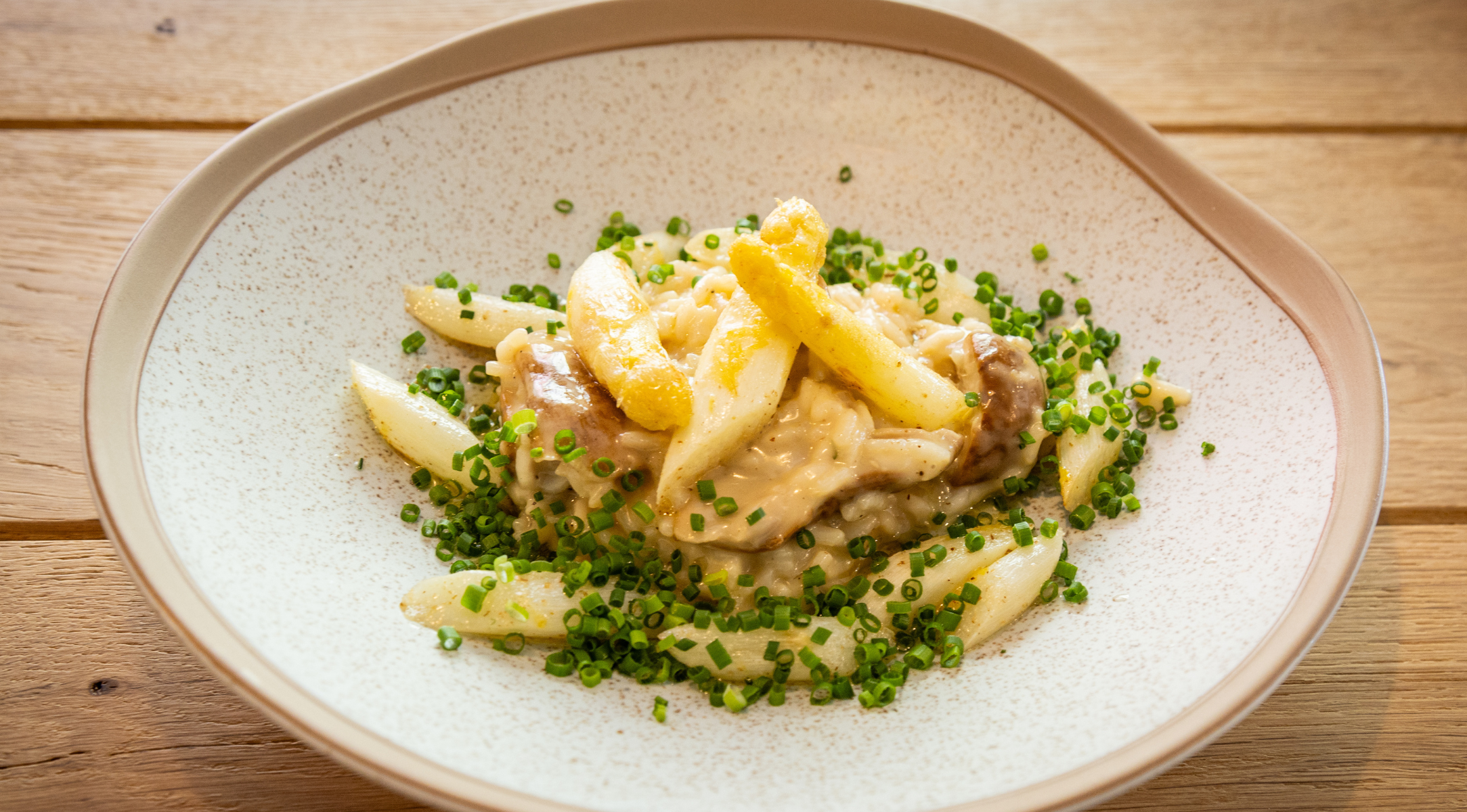 A meticulously plated dish of creamy pasta with golden fries and fresh green herbs rests on a pristine white ceramic plate atop a wooden table, exemplifying the refined presentation achievable with Fissler’s precision-engineered cookware.