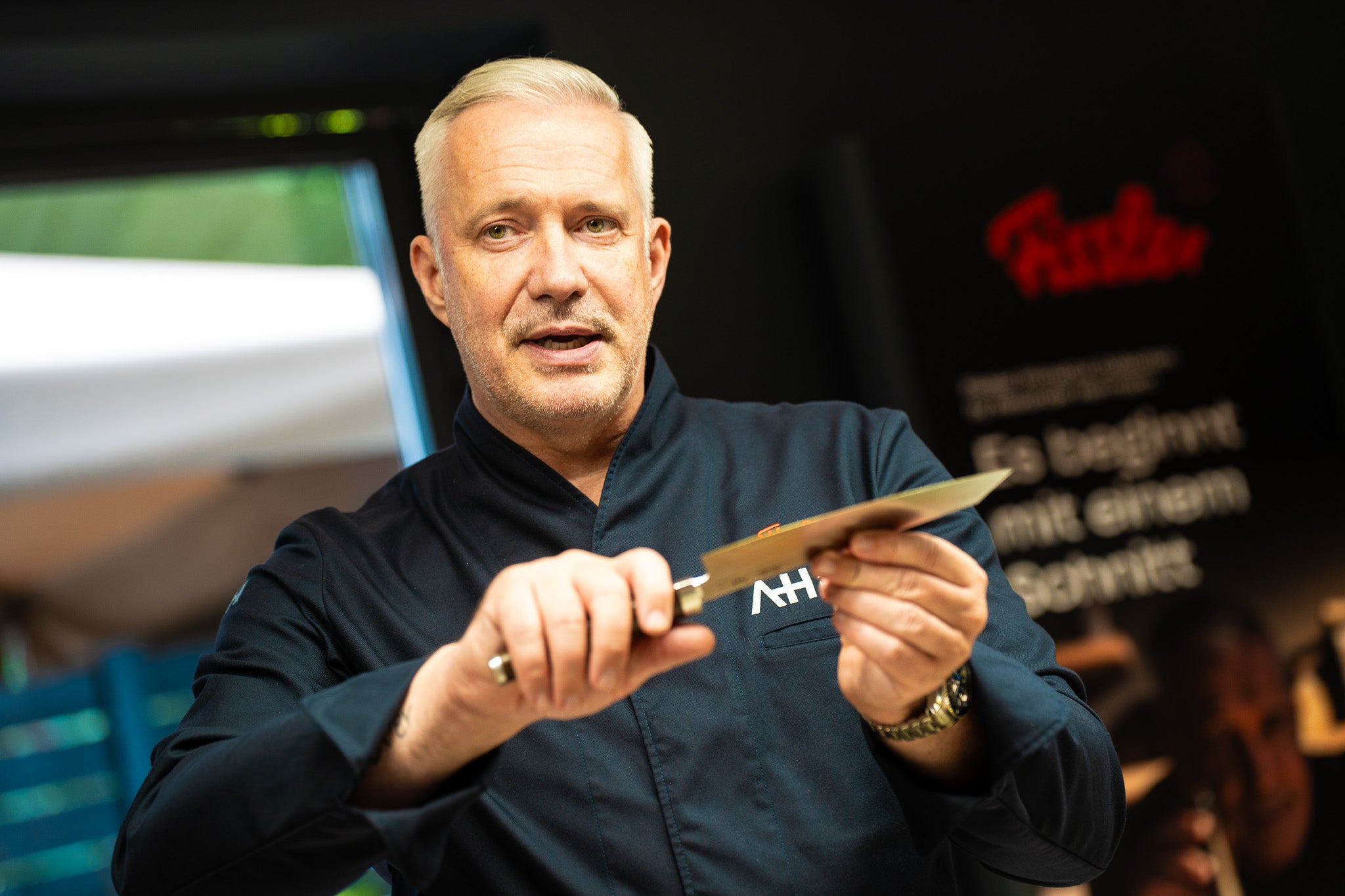 Ein Koch in einer dunklen Jacke präsentiert ein hochwertiges Fissler-Küchenmesser und unterstreicht damit die deutsche Präzision und Qualität in einer hellen Wohnküche.